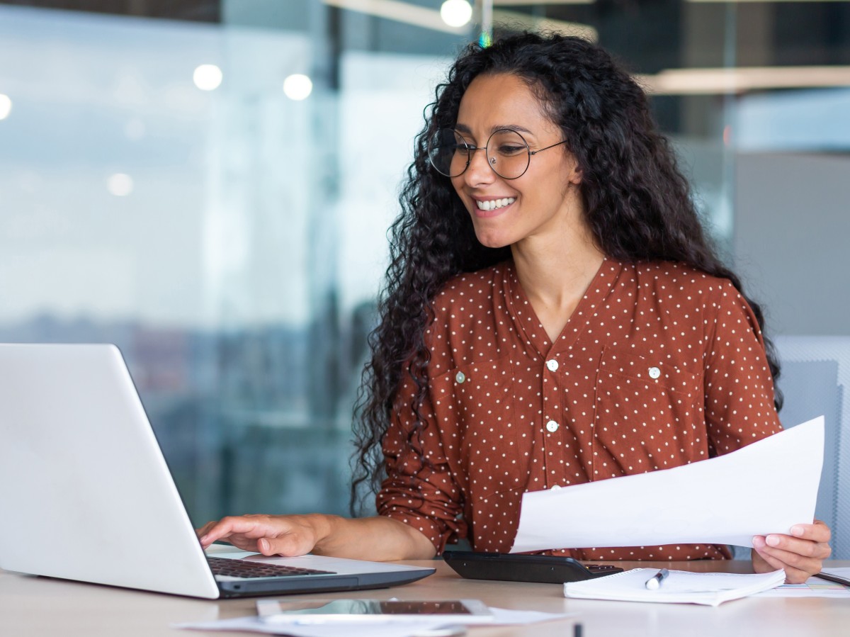 Betriebswirtin sitzt vor Laptop mit Ausdruck in der Hand