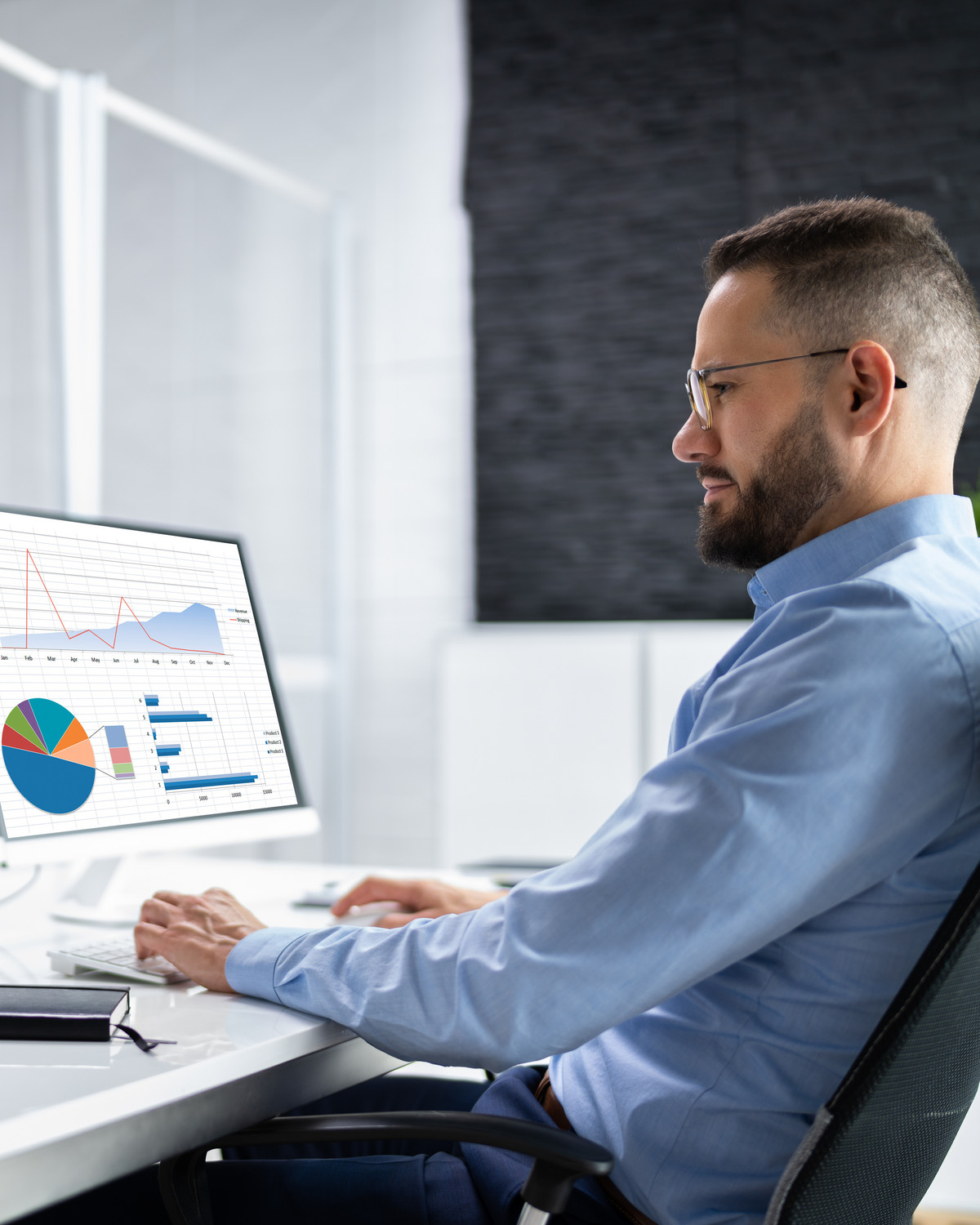 Fachwirt im IT-Commerce sitzt vor Monitoren und analysiert Online-Verkaufszahlen