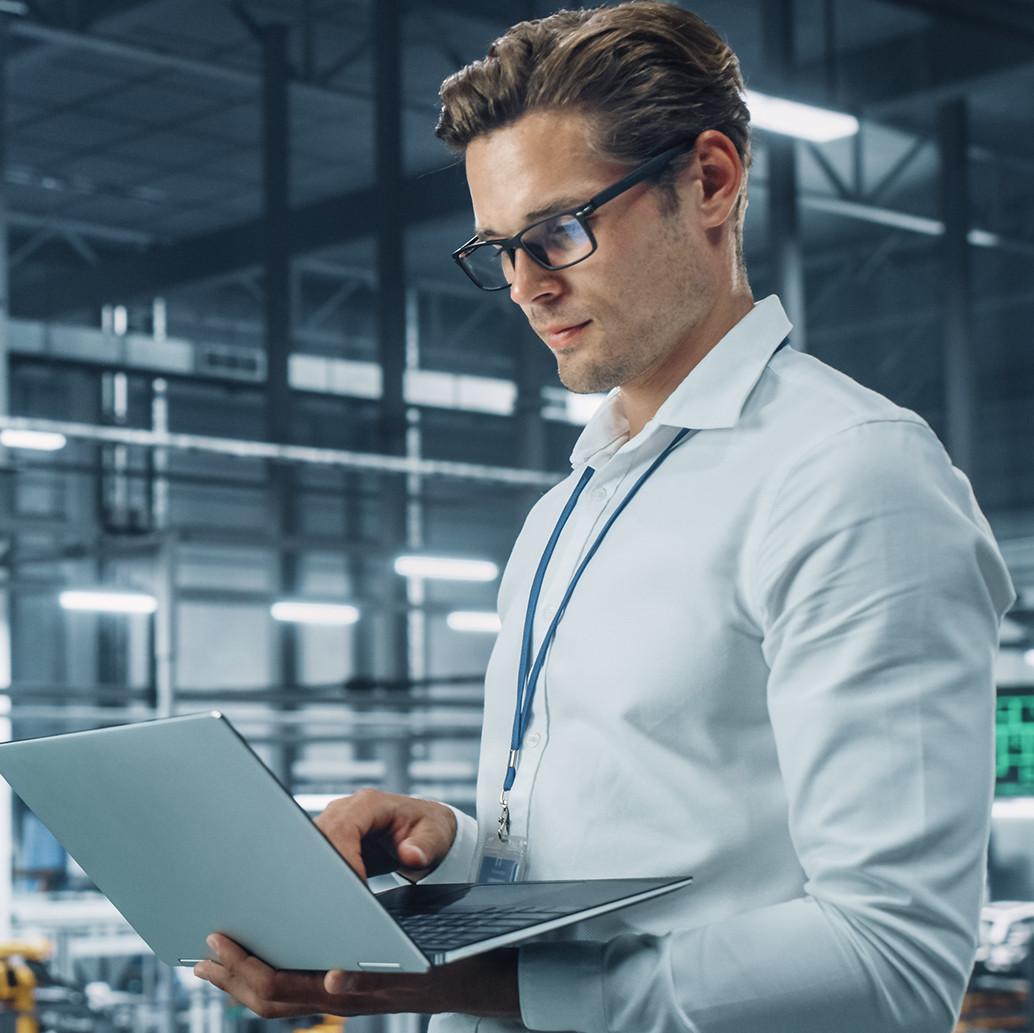 Geprüfter Industriefachwirt führt Audit am Laptop in Produktionshalle durch