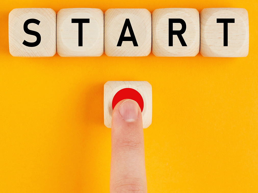 Würfel, auf denen aneinandergereiht START steht und ein Finger der einen Startknopf drückt